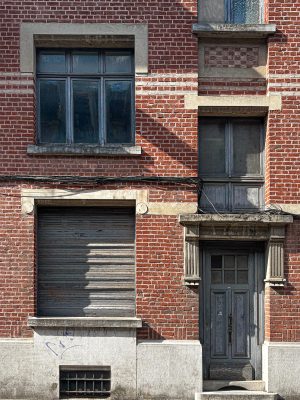 Facade of an old brick bourgeois building with a weathered wooden door, shuttered window, and stone details.