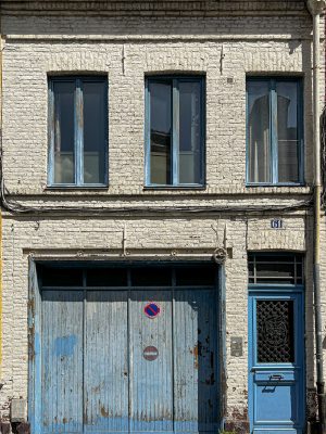 A small white brick house with blue shutters, whose charm still shines through despite the wear.